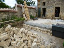 Aménagement d'une terrasse d'une ancienne écurie. Remblai au niveau des seuils, fondations, murets en parpaings et moellons issus de l'écurie, carrelage en pierre multiformat, spots encastrés dans la dalle et escalier en pierre et béton. (Pendant)