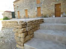 Aménagement d'une terrasse d'une ancienne écurie. Remblai au niveau des seuils, fondations, murets en parpaings et moellons issus de l'écurie, carrelage en pierre multiformat, spots encastrés dans la dalle et escalier en pierre et béton. (Après)