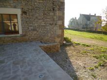 Aménagement d'une terrasse d'une ancienne écurie. Remblai au niveau des seuils, fondations, murets en parpaings et moellons issus de l'écurie, carrelage en pierre multiformat, spots encastrés dans la dalle et escalier en pierre et béton. (Après)